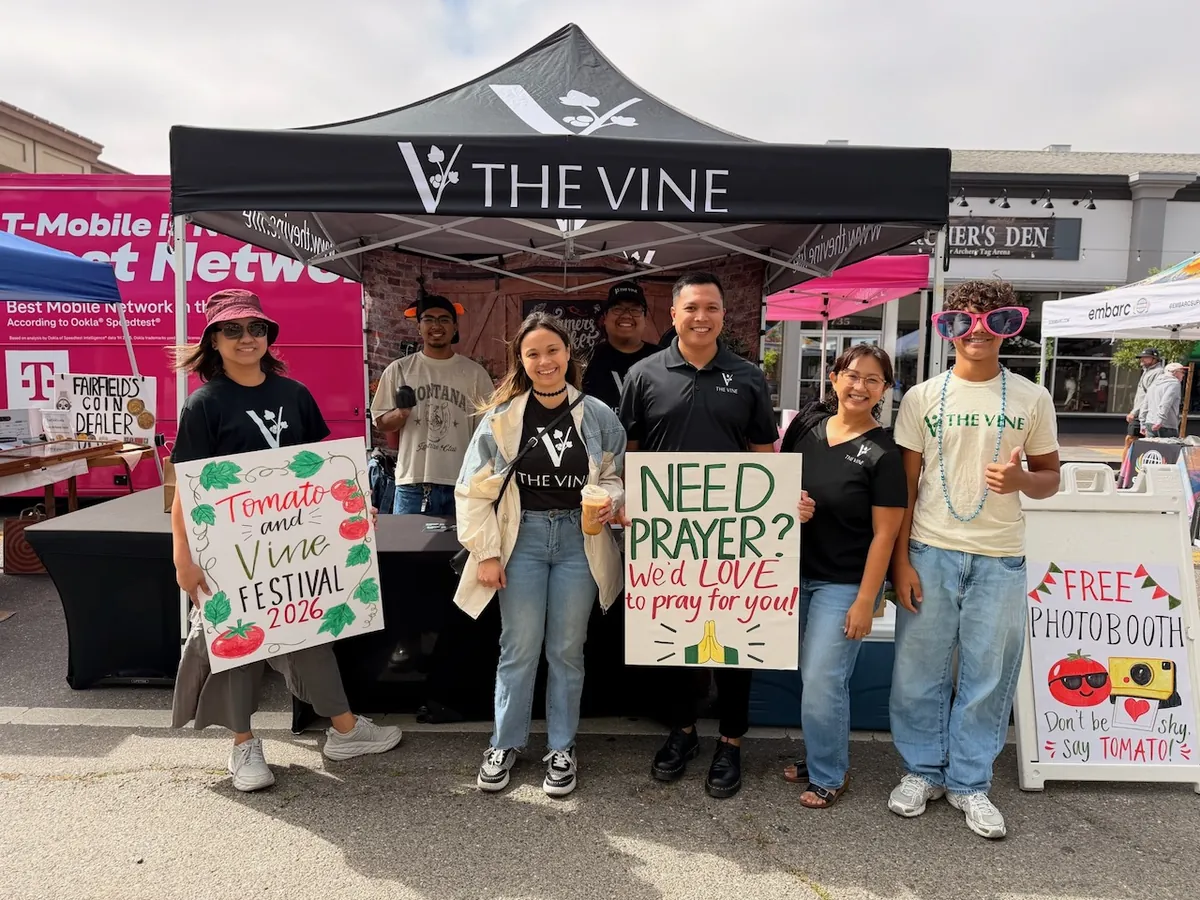 Volunteers holding hand-painted signs reading “Need prayer? We’d love to pray for you” and “Free photo booth” at the festival booth