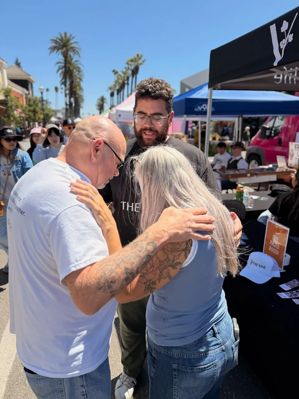 Two volunteers praying with a festival guest beside the free photo booth table